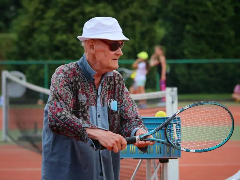 Starszy mężczyzna trzymający rakietę tenisową, uśmiechający się z pasją do sportu.