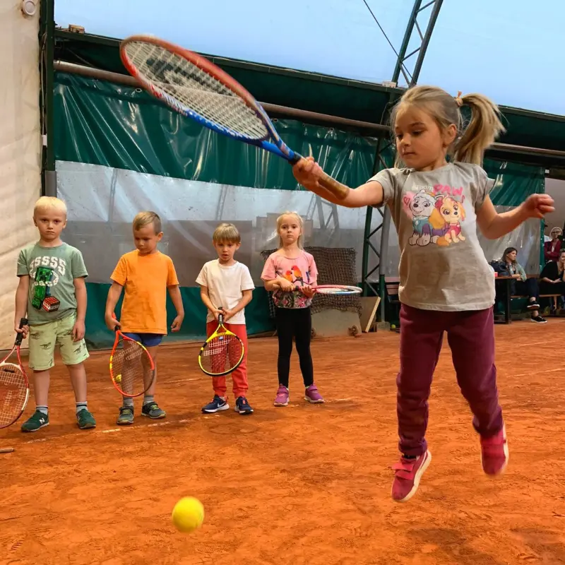 Młoda dziewczynka uderza piłkę tenisową rakietą, skupiona na grze na korcie tenisowym.