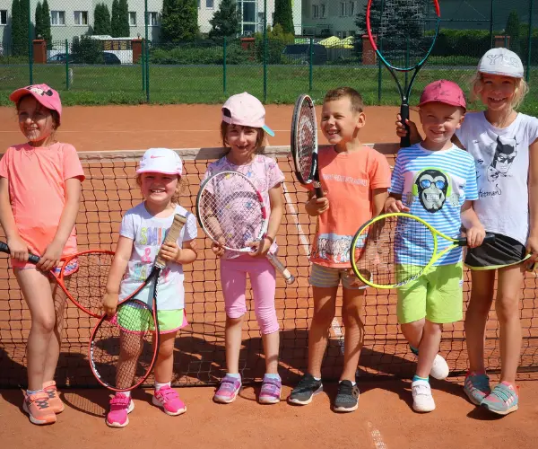 Grupka małych dzieci z rakietami tenisowymi pozująca do zdjęcia.